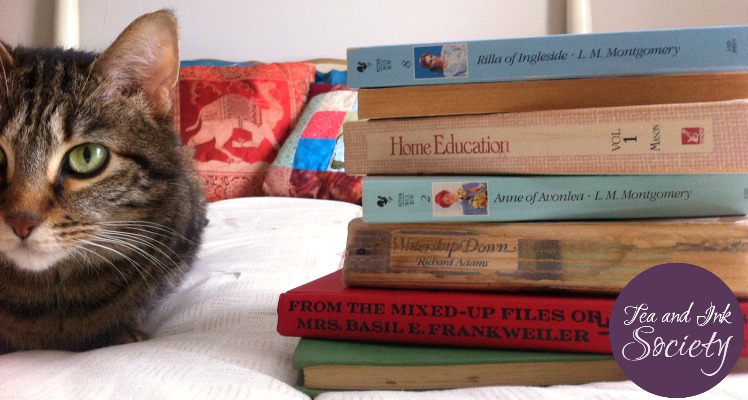 Stack of books on a bed next to a green-eyed cat