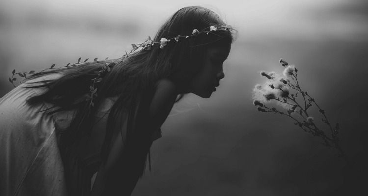 Black and white photo of a girl with a flower crown bending down to look at wildflowers