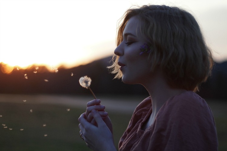 Profile of girl blowing dandelion flower at sunset