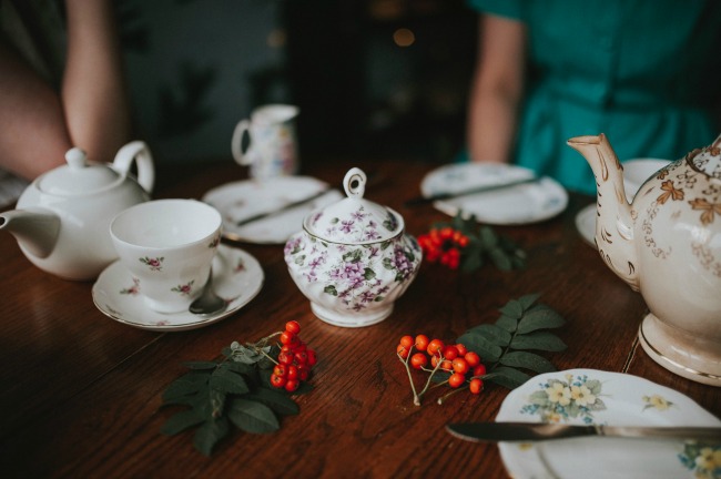 Eclectic china tea cups, saucers, and teapots, with greenery
