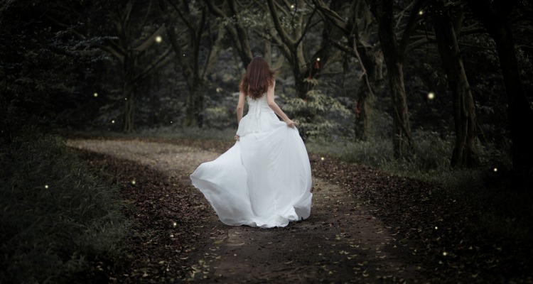Girl in a white ball gown running through a dark yet sparkling forest