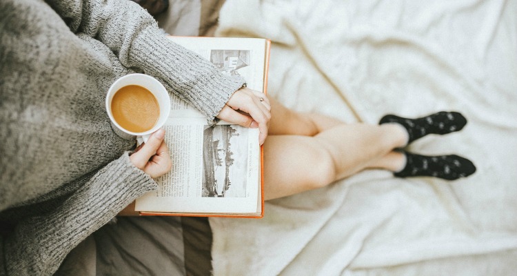 Woman in a cozy sweater reading a book with a cup of coffee