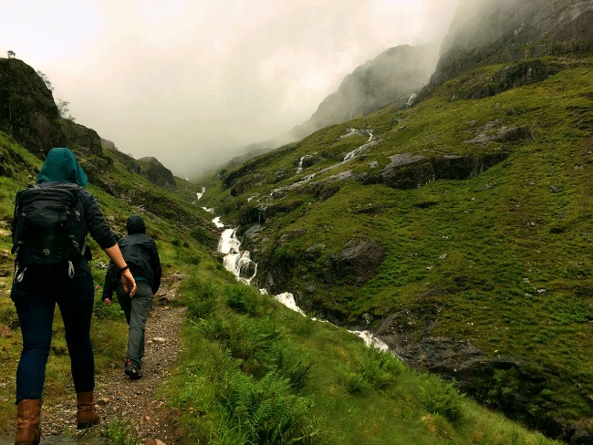 Two people hiking in Scotland through a misty valley