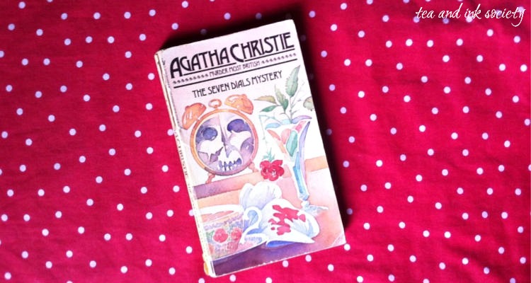 Paperback copy of The Seven Dials Mystery by Agatha Christie on a red blanket with with spots