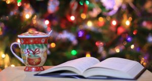 Open book and Christmas mug in front of a Christmas tree