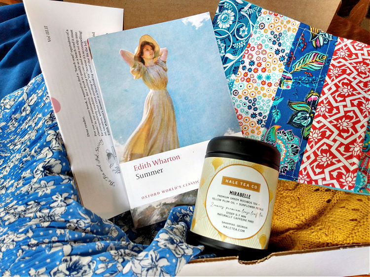 Book and tea subscription box with copy of Summer by Edith Wharton, tin of Mirabelle tea from HaleTea Co. and brightly-patterned mug rug.