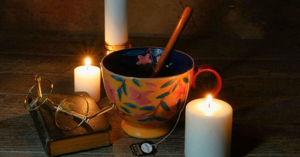 Cozy candlelit still life photograph with tea cup, book, and reading glasses
